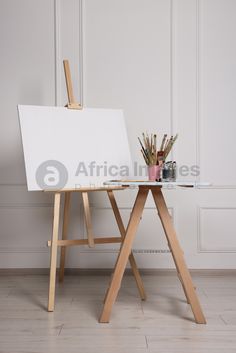 an easel with paint and pencils on it in front of a white wall