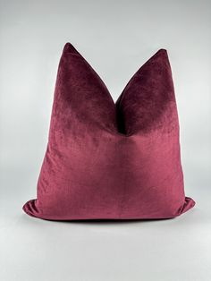 a purple pillow on a white surface with a grey background and the bottom part of the pillow has a deep red color