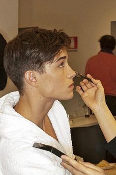 a woman is getting her make - up done by another person in a bathroom with other people