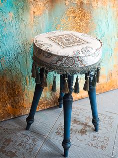 a stool with tassels on it sitting in front of a wall and floor