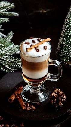 a cup of hot chocolate and cinnamon on a black plate next to christmas tree branches