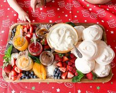 a platter filled with fruit and dips on top of a red table cloth