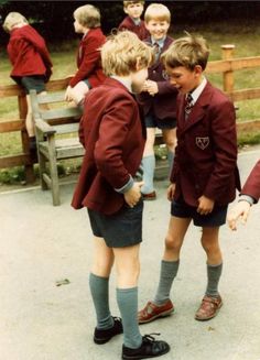 two young boys in school uniforms talking to each other on a bench with others behind them