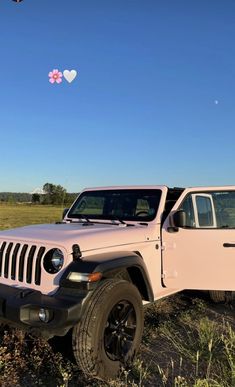 a pink jeep parked in a field with a heart shaped balloon flying over the top