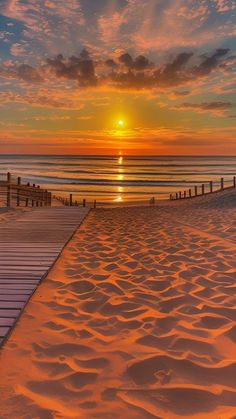 the sun is setting over the ocean and beach with a boardwalk leading into the water