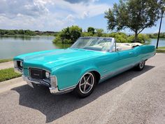 an old blue convertible car parked on the side of the road next to a lake