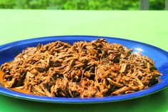 a blue plate filled with shredded meat on top of a green tablecloth next to a cup of coffee