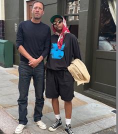 two men standing next to each other on a sidewalk