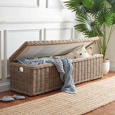 an open wicker trunk on the floor next to a potted plant and slippers