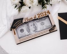 a class of 2020 money bill with graduation cap on top and flowers in the background