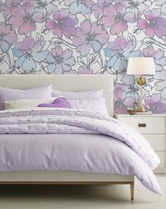 a bed with purple and blue flowers on the wall in front of it, next to a night stand