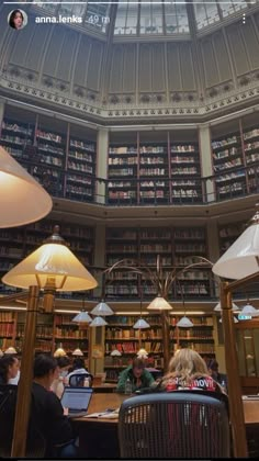 people sitting at tables in a library with lots of bookshelves and lamps on the ceiling