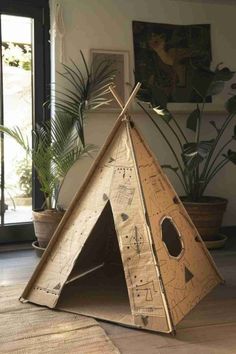 a wooden teepee sitting on top of a floor next to a potted plant