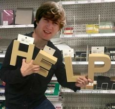 a young man holding up two cardboard letters that spell the word hlp in front of him