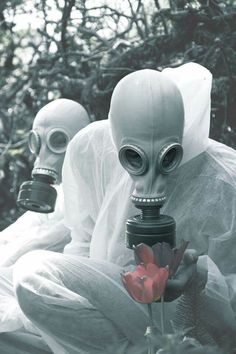 three people dressed in white with gas masks and holding a camera