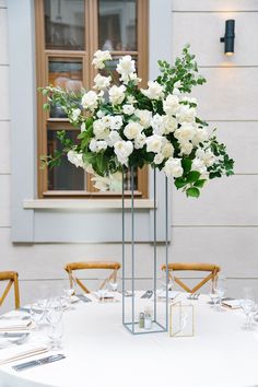 two tall vases filled with white flowers on top of a table