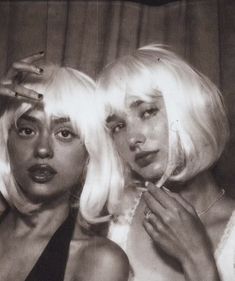 two women with blond hair are posing for the camera and one is brushing her teeth