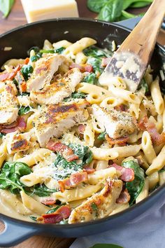 a skillet filled with pasta, chicken and spinach on top of a wooden table