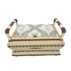 a wicker ottoman with wooden handles and cushion on the top, sitting in front of a white background