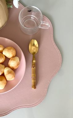 a pink plate with some food on it and a gold spoon sitting next to it