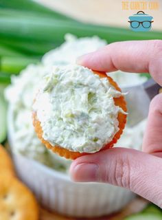 a hand holding a small cracker filled with cream cheese and cucumber sticks