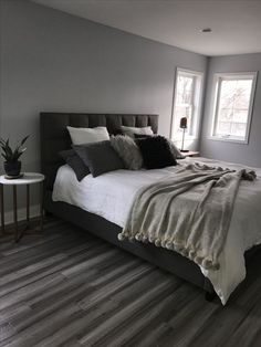 a large bed sitting next to two windows in a bedroom on top of a hard wood floor