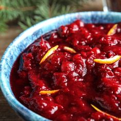 a blue bowl filled with cranberry sauce on top of a wooden table next to an orange slice