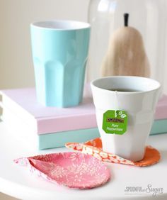 two cups are sitting on a table next to some books and a teapot with a pear in the background