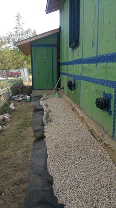 a green building with blue tape on the side and some rocks in front of it