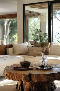 a wooden table with a vase on it in front of a living room couch and windows