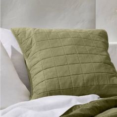 a bed with white sheets and green pillows