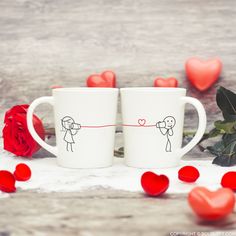 two coffee mugs with stick figures drawn on them next to red roses and hearts