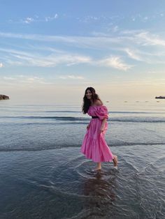 a woman in a pink dress is standing in the water at the beach and smiling