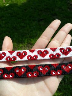 two red and black hearts on white beaded wristbands, one being held by a hand