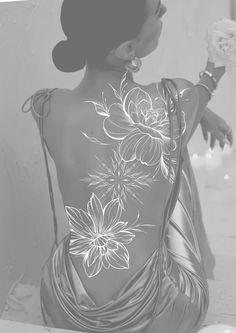 the back of a woman's body with flowers painted on it, holding an object in her hand