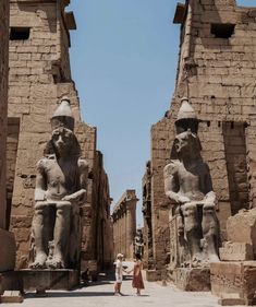 two people are standing in front of some ancient statues at the entrance to an egyptian temple