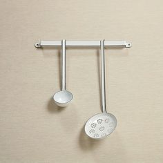 two metal spoons hanging from hooks on a beige wall next to a white bowl