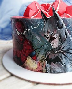 a batman themed cake on a plate with a red bow in the middle and spiderman wrapping around it