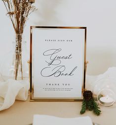 a sign that says guest book next to a vase with flowers and candles on the table