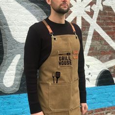 a man standing in front of a brick wall wearing an apron with the words grill house on it