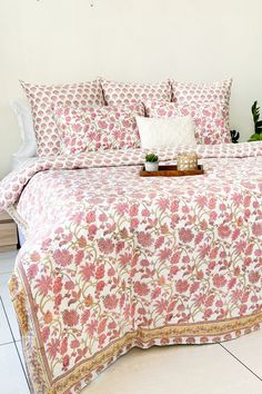 a bed covered in pink and white floral bedspread with two pillows on it