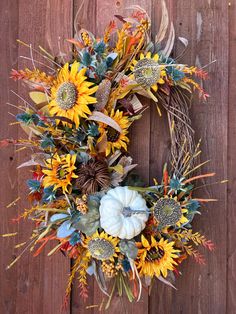 a wreath with sunflowers and other flowers hanging on a wooden fence next to a white pumpkin