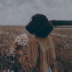 a woman standing in a field holding a bouquet of daisies and looking at the sky