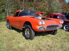 an orange car parked in the grass next to another red car and some other cars