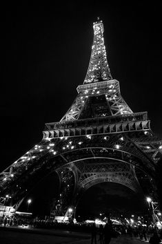 the eiffel tower lit up at night in black and white with people walking around