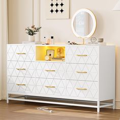 a white dresser with gold handles and drawers in front of a mirror on the wall