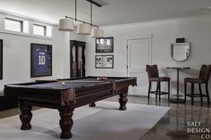 a pool table sitting in the middle of a living room next to two bar stools