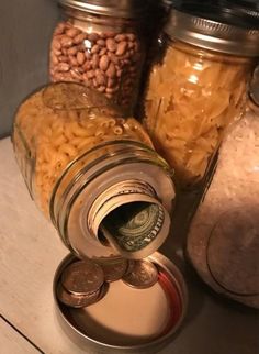 jars filled with different types of food sitting on top of a wooden table next to coins