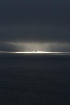 the sun is shining through dark clouds over the ocean