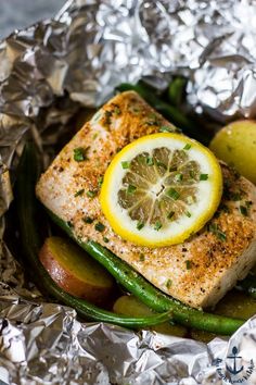 a piece of fish with lemon and green beans in foil on a plate next to an apple